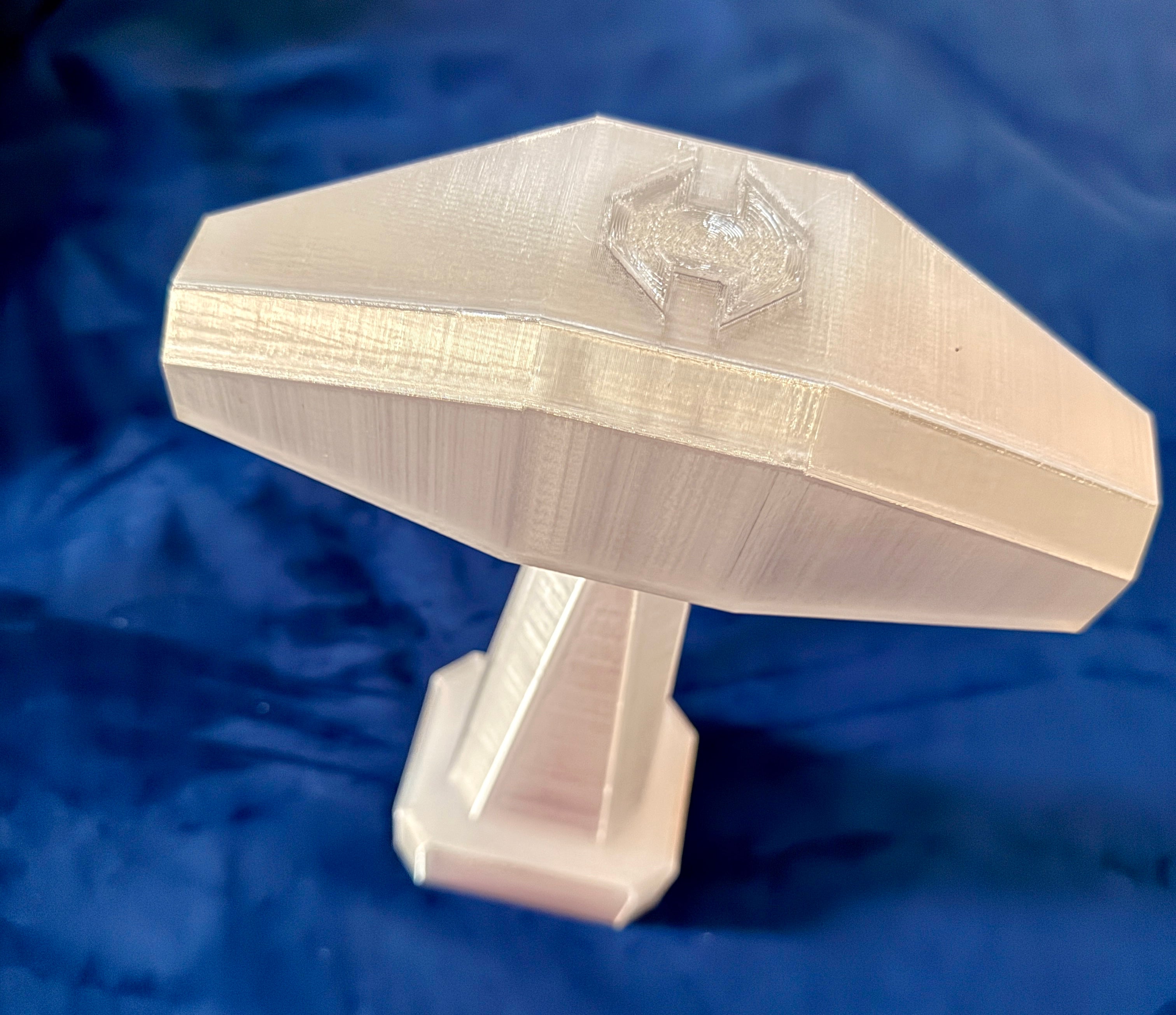 Top down view of the Thor hammer in metallic gold on a velvet blue background.