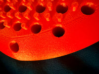 Close-up of a red Hera paddle with prongs and circular holes on a dark background.