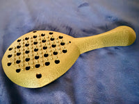 Hera paddle in metallic gold on a purple background.