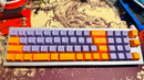 Mechanical keyboard with orange and purple keycaps on a decorative surface